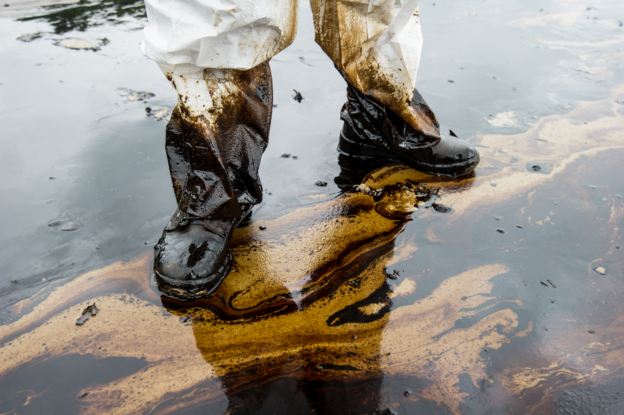 A person in a dirty hazard suit standing in a puddle of oil.