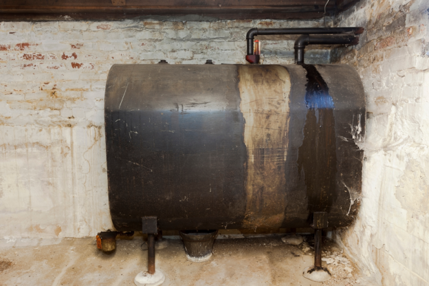 A rusted and potentially leaking oil tank inside a cellar.