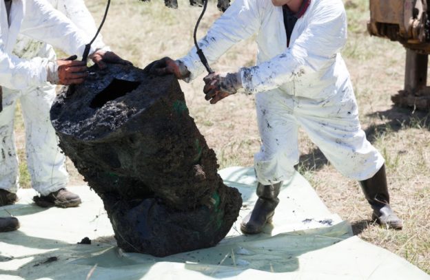 Two men in hazard suits cleaning out solidified oil.